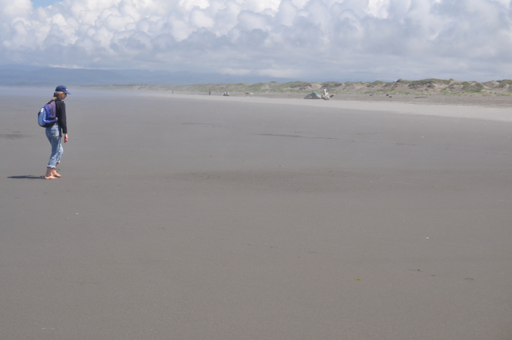 hiker walks barefoot on broad sandy beach at low tide